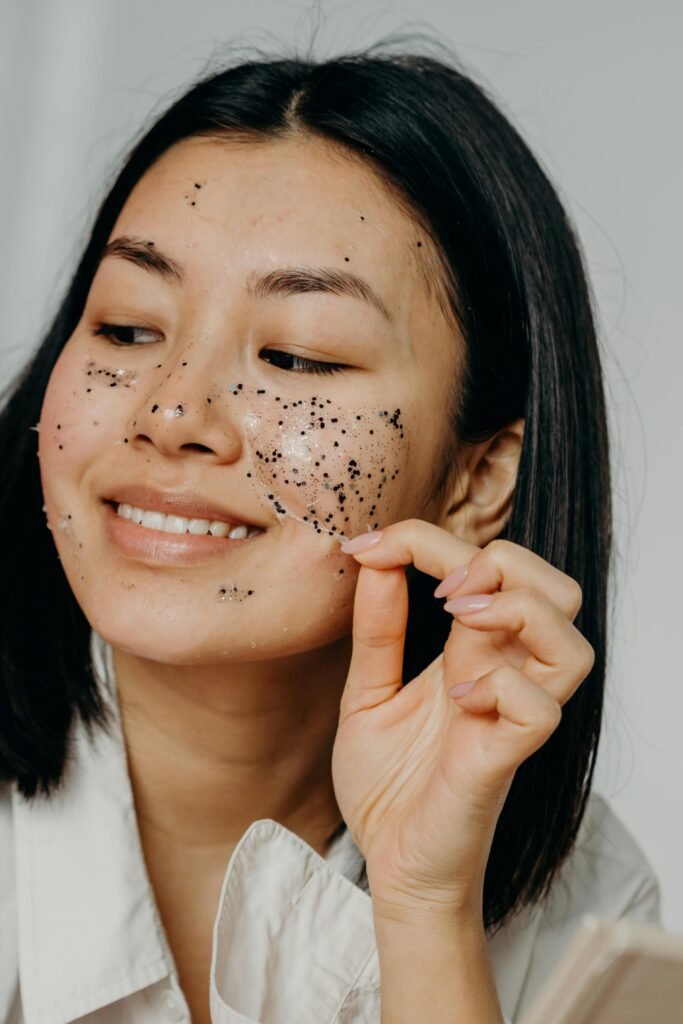Smiling Asian woman applies an exfoliating mask for healthy skincare routine.