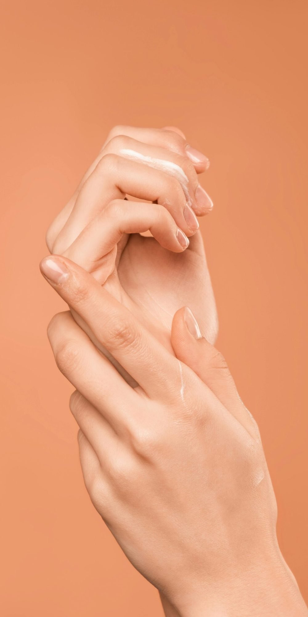 Close-up of hands with oil on peach background, emphasizing skincare and wellness.